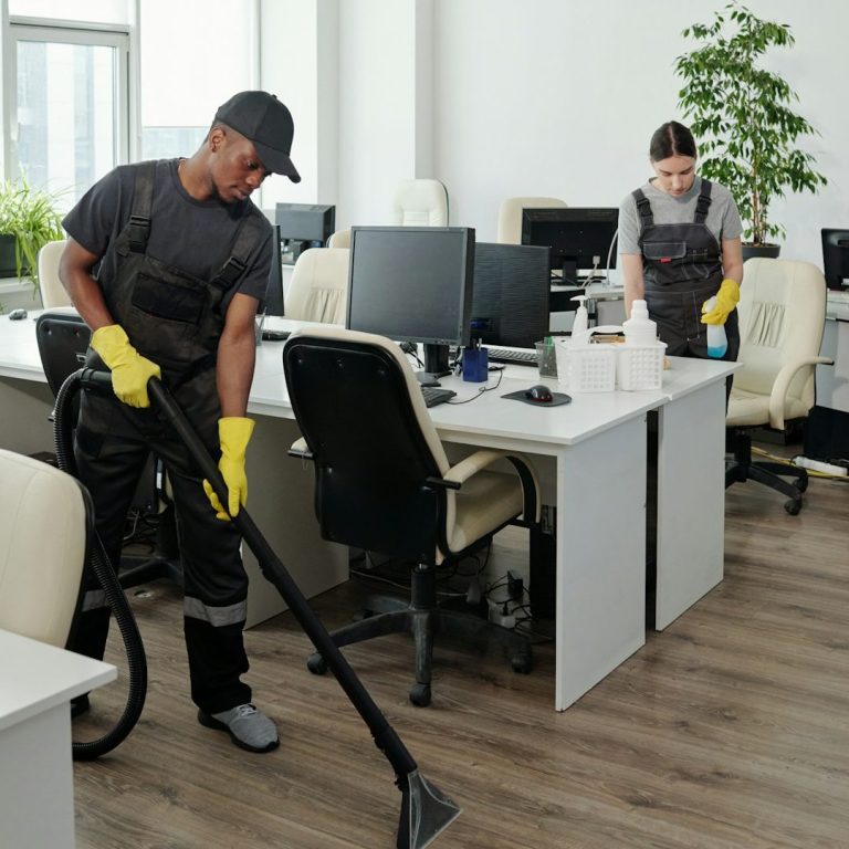 Büro Zwei Reinigungskräfte säubern ein modernes Büro mit Staubsauger und Reinigungsmitteln.